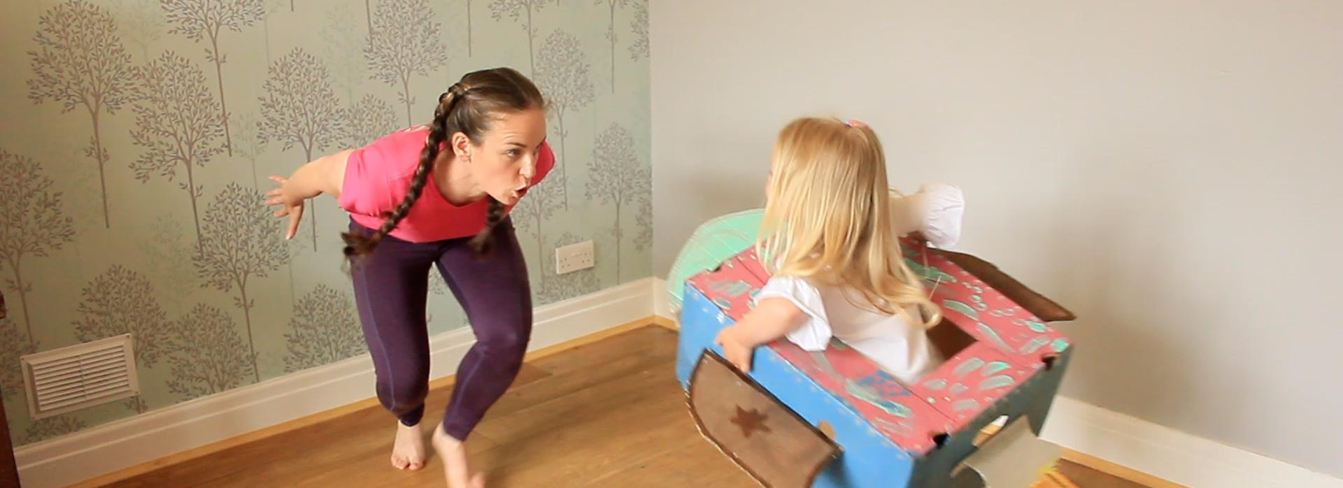 A woman and child dance together. The child is inside a painted carboard box that looks like a rocket.