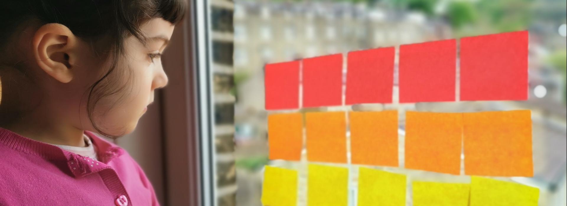 A young girl plays with coloured post-its on a window