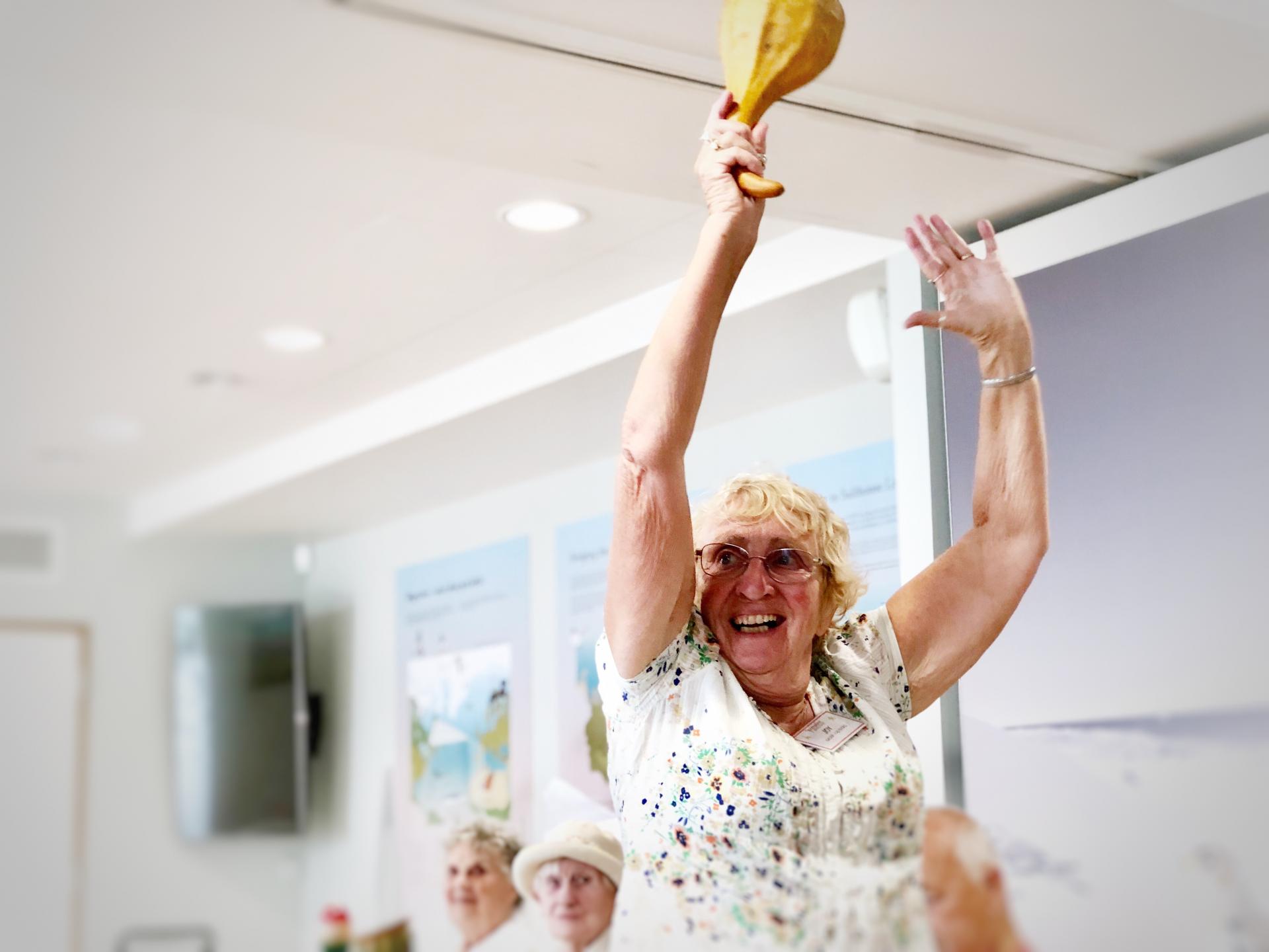 Short old lady holding a yellow object in the air with both hands up.