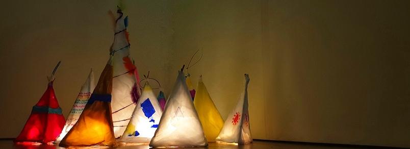 a collection of homemade paper lanterns in warm colours, in the corner of a darkened room