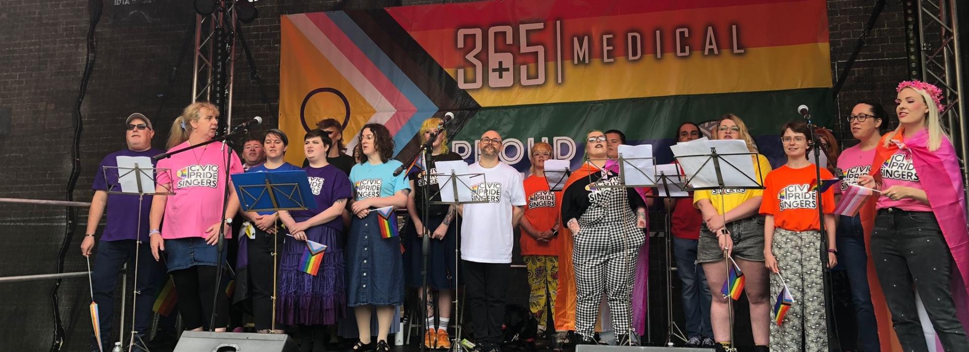 photo of a choir standing on a stage with a large pride banner behind them