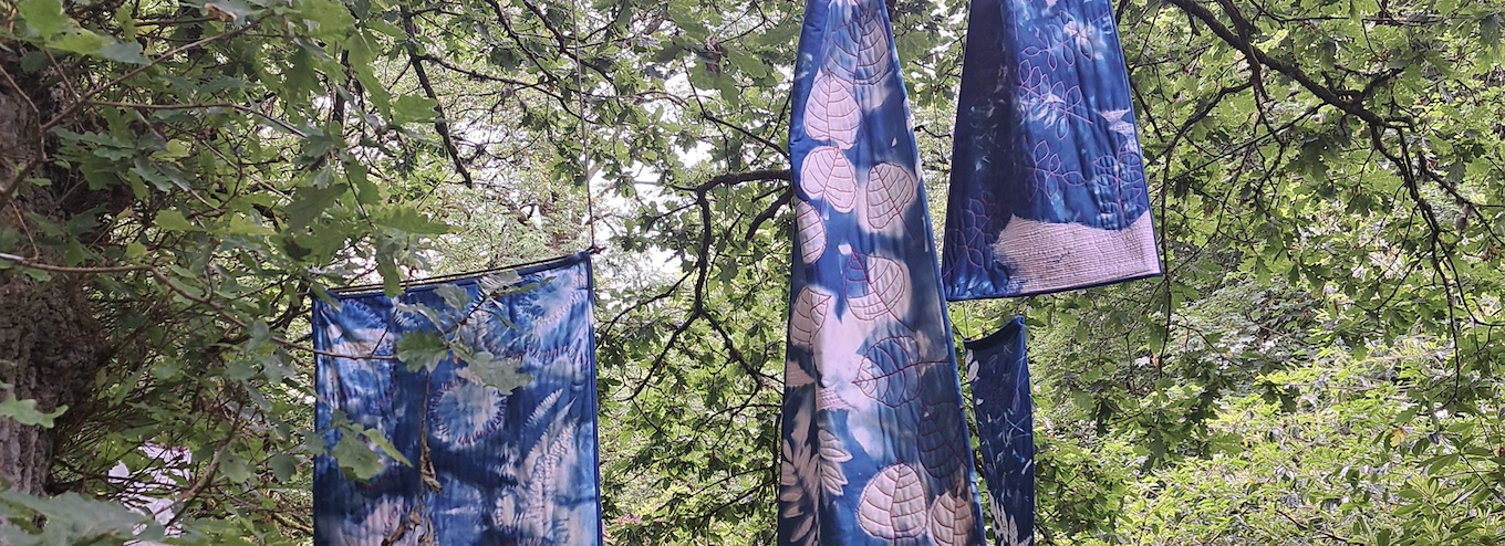 Three blue and white tie dye fabric pieces hanging from trees
