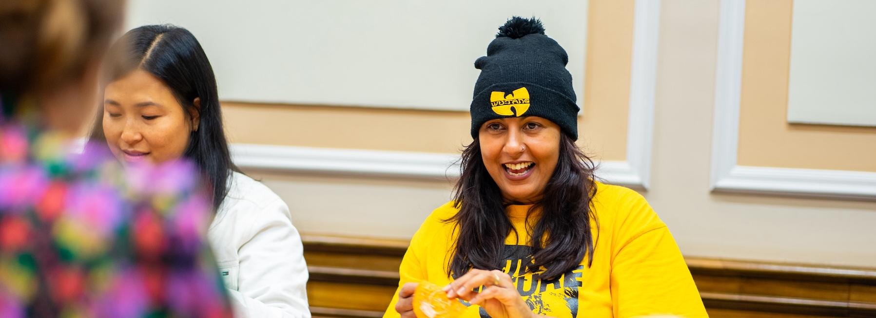 3 women sit at a table full of craft materials making a textile