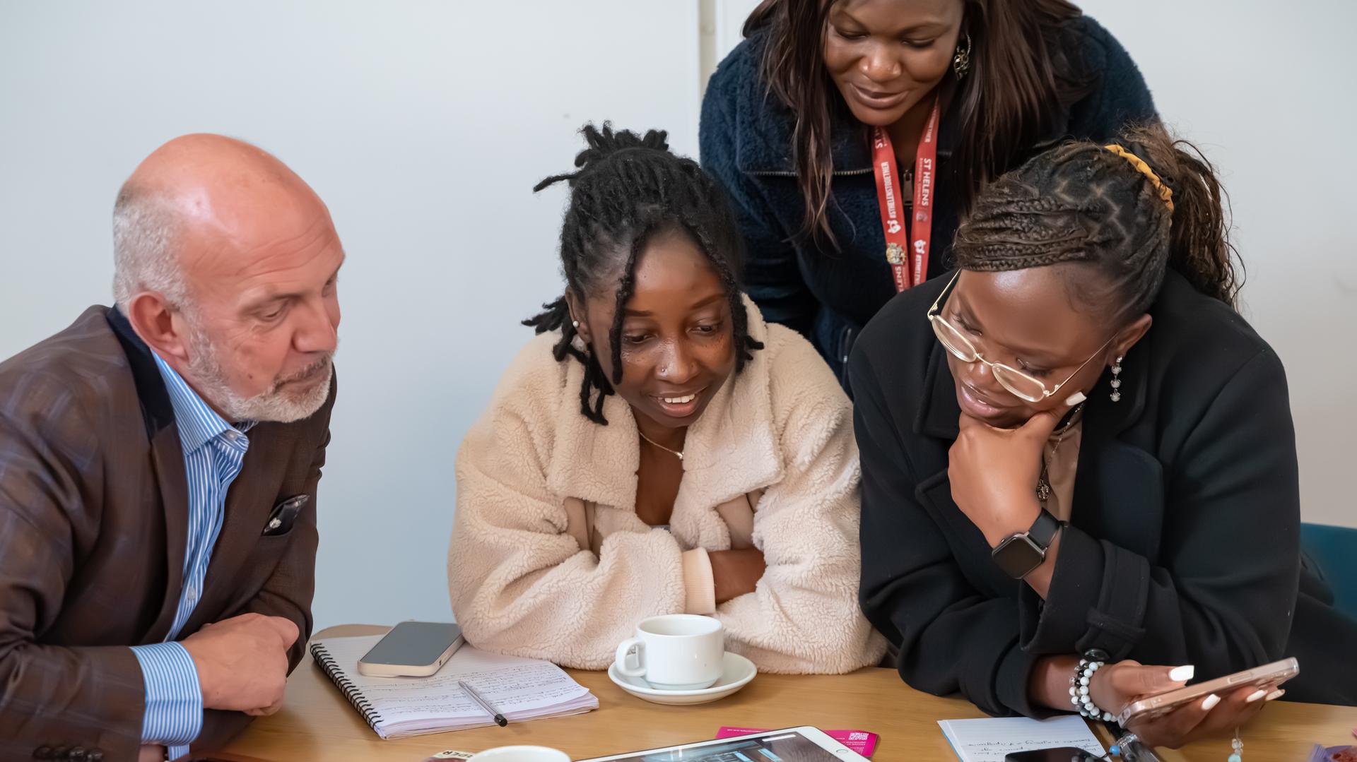 multiple people sitting down and one person standing up at a table looking at written materials