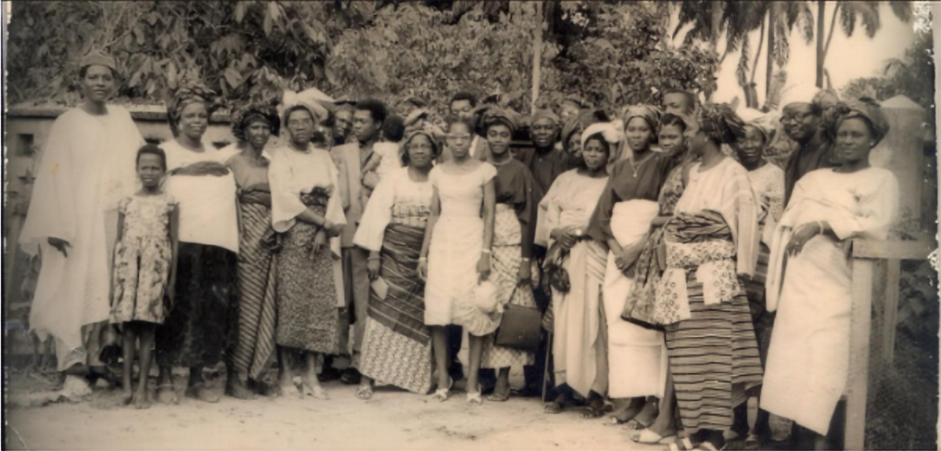 A large group of women and men posing for a group picture  against a natural backdrop in black and white