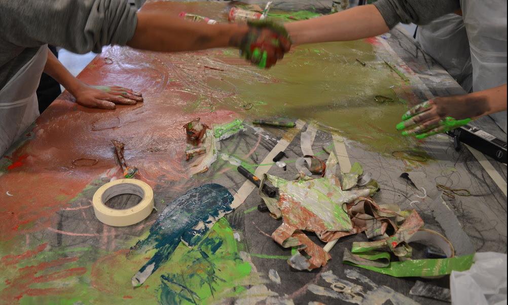 Photo of two people shaking hands, with their hands covered in paint after an art workshop