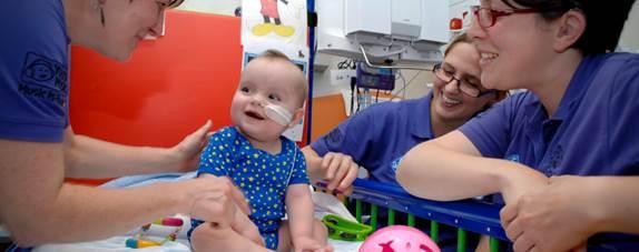 Nurses surround a baby in hospital, smiling