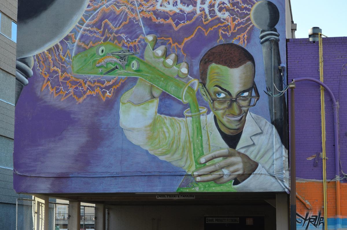 wall graffiti image of a man in a lab coat pouring green chemicals into a glass vessel