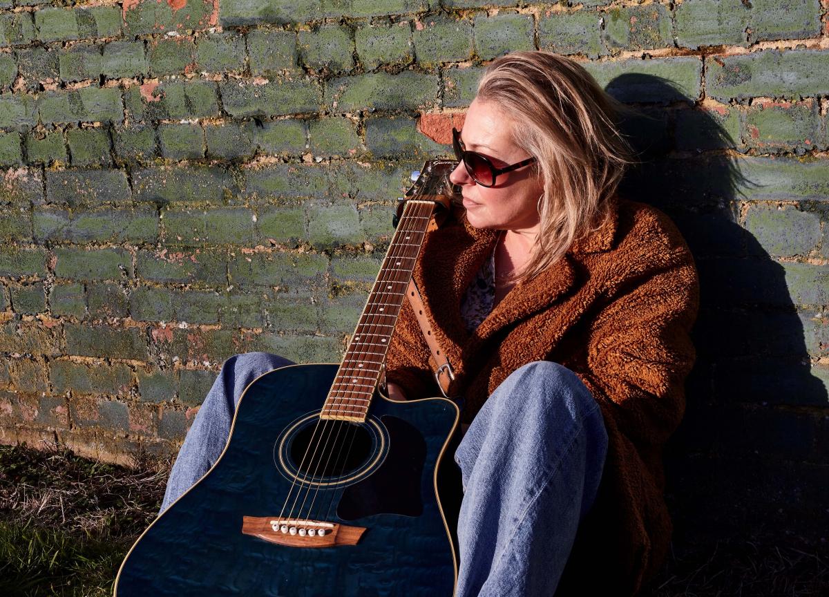 Tina Blaber with guitar against a wall