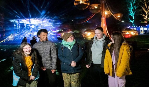5 people stand smiling in front of a light display, outside at night