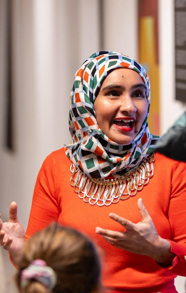 close-up photo of a woman in a colourful headscarf and orange top speaking animatedly in a group setting