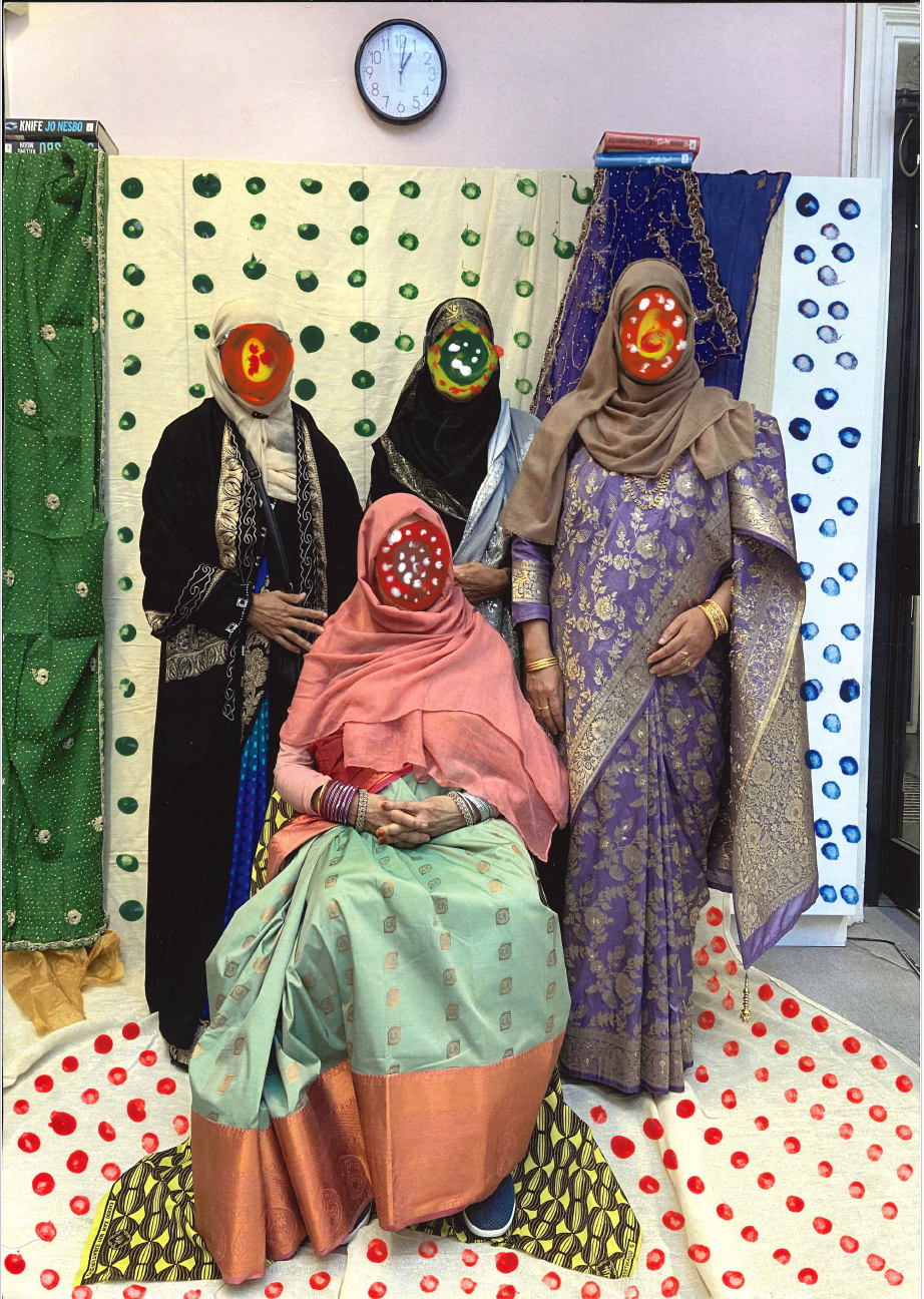 Women sitting and standing in front of polka dot background wearing vibrantly coloured saris