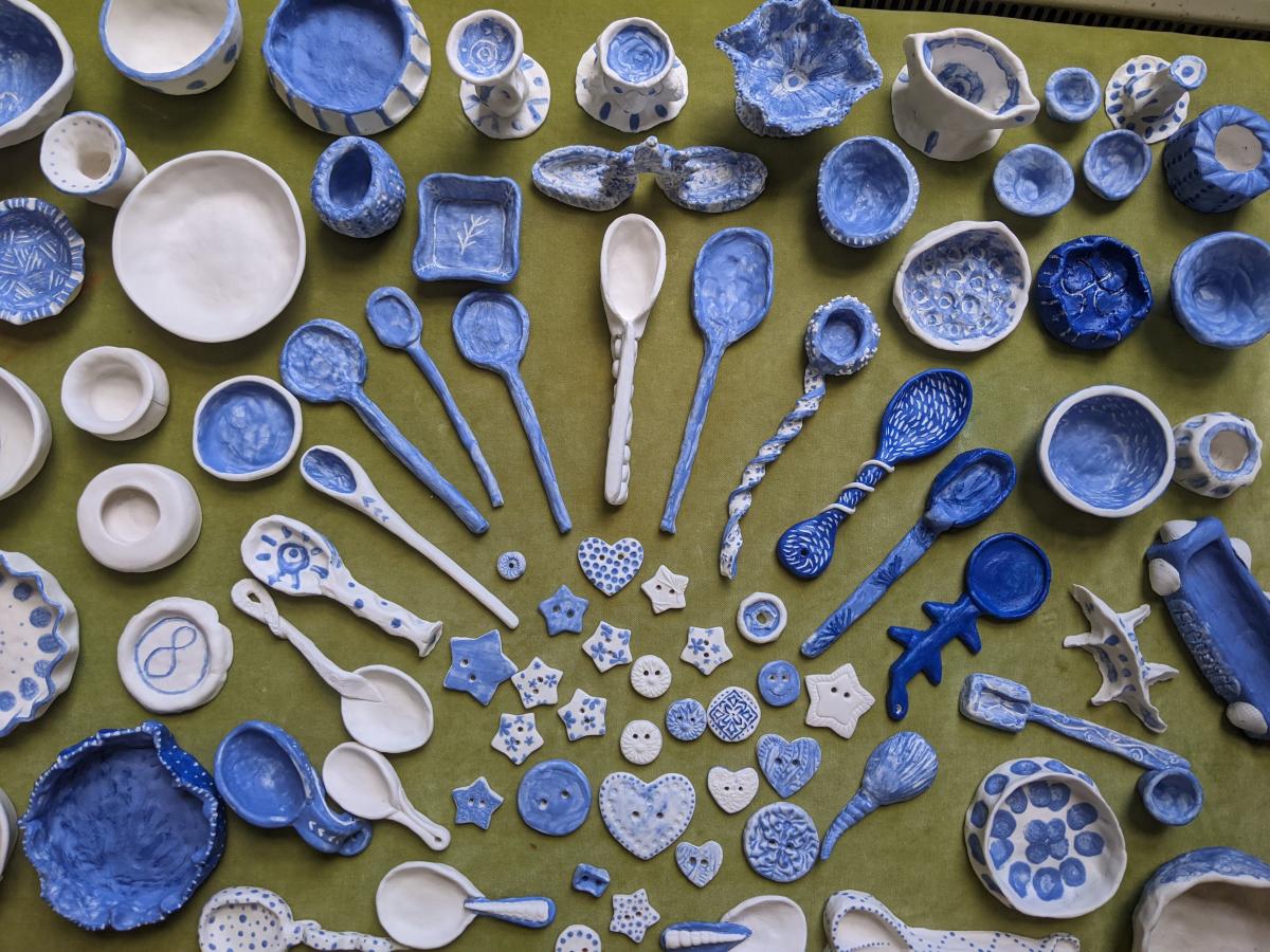 a collection of handmade blue-and-white spoons, bowls and buttons photographed from above arranged in a fan shape on a green table