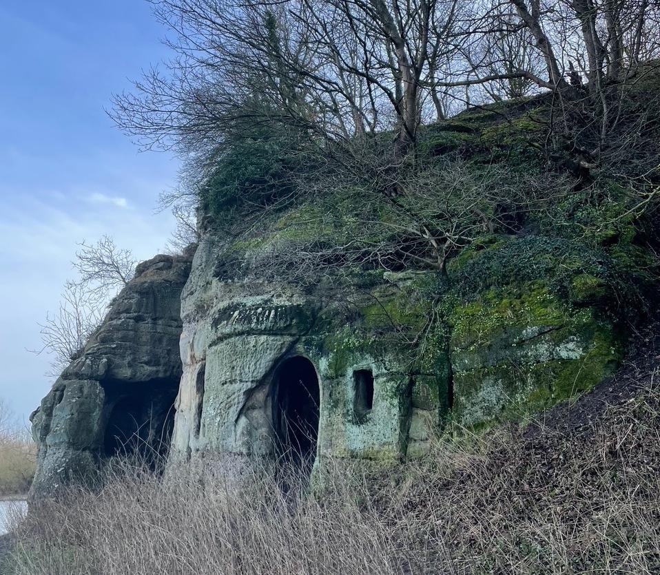 photo of a cave in a sandstone outcrop in winter with grasses and water surrounding it