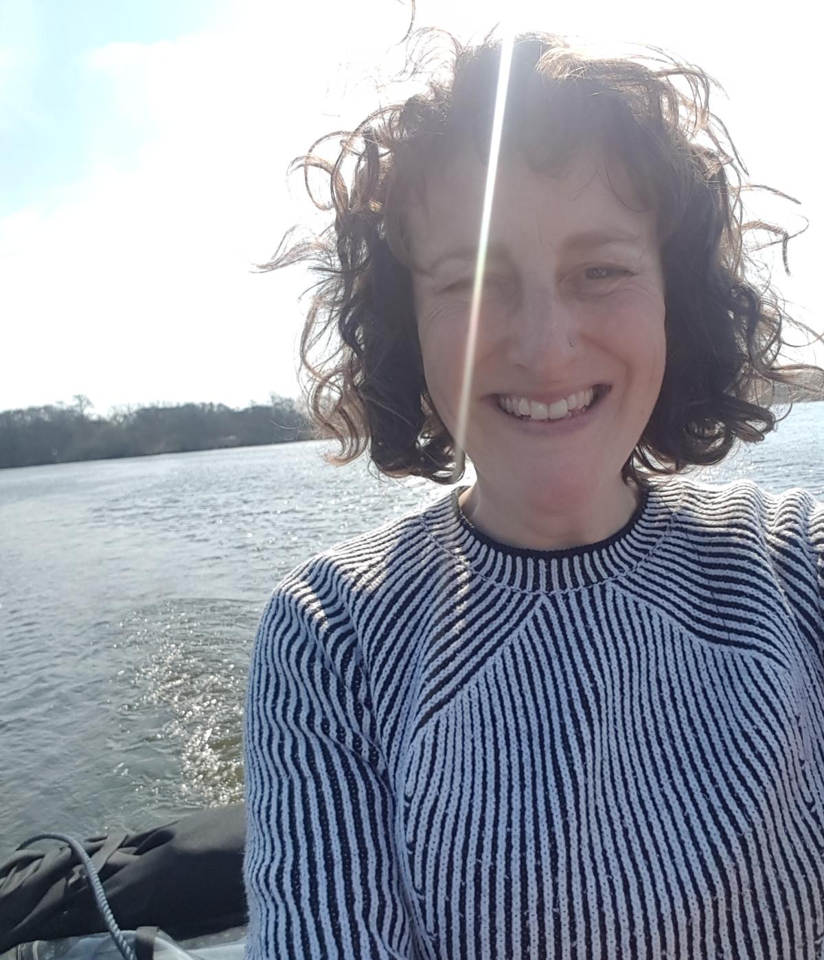 curly haired woman wearing a striped jumper smiling against a sea facing background