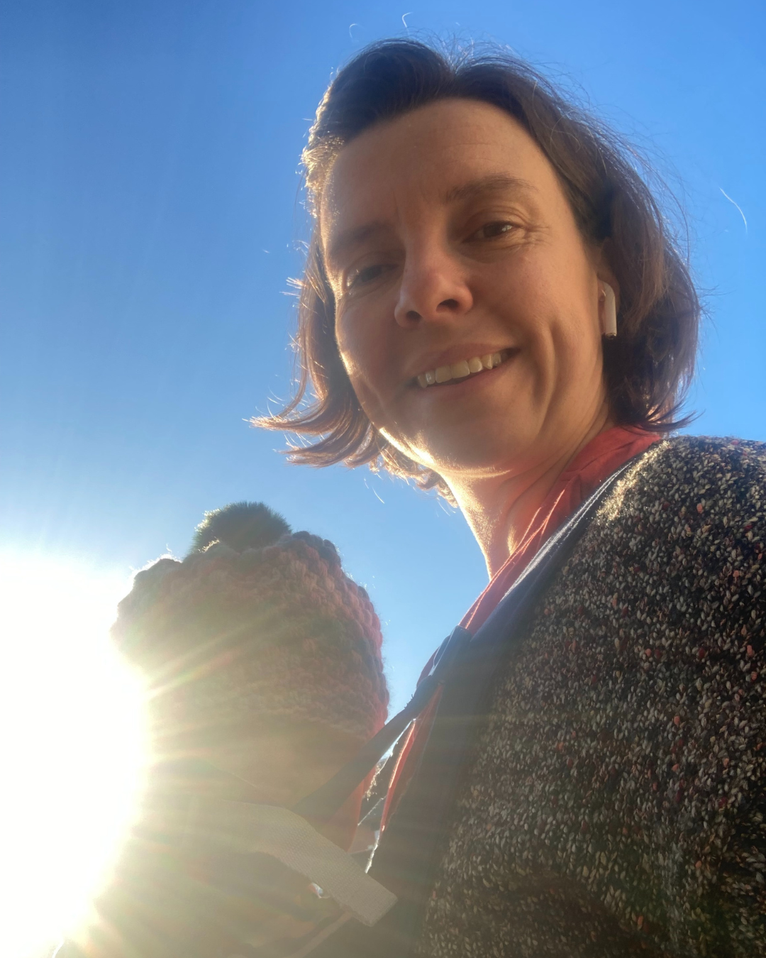 A white woman with shoulder length brown hair wearing a wooly jumper smiling at the camera standing sideways on against a brilliant blue background