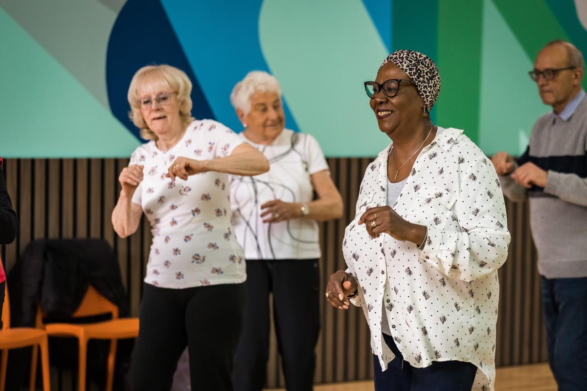 Older women and men wearing white patterned clothing dancing in a hall 