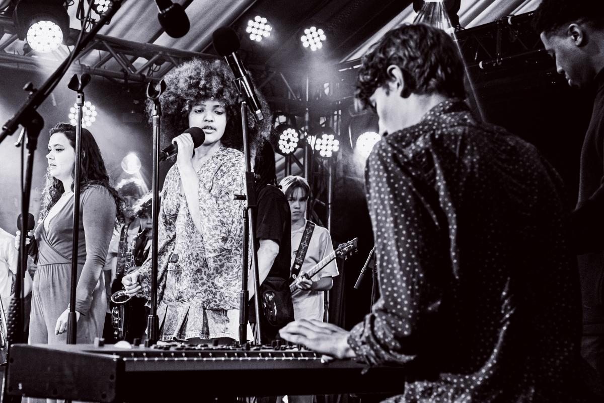 a group of young people on stage singing and playing musical instruments 