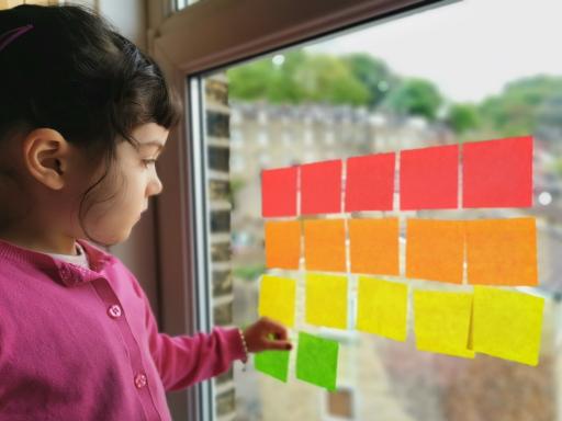 A young girl plays with coloured post-its on a window