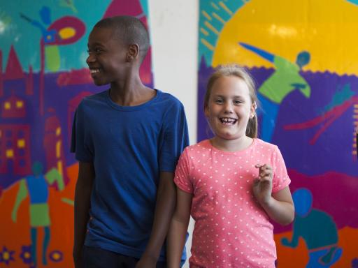 two young carers standing and smilling in front of a colourful artwork in the background