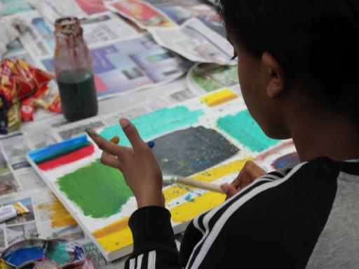 A young girl photographed from over her shoulder, painting a colourful picture
