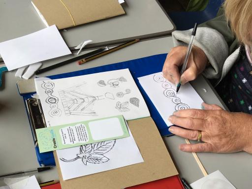 An image of a white woman's hands doodling on a card on a blue clip board