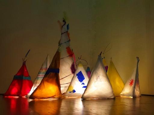 a collection of homemade paper lanterns in warm colours, in the corner of a darkened room