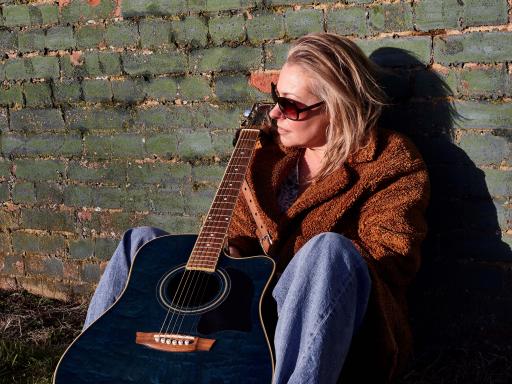 Tina Blaber with guitar against a wall