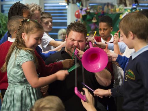 Musician playing a pink trombone surrounded by school children