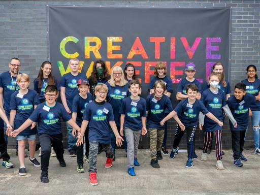 A group of young people and staff stand in front of a wall with the words Creative Wakefield in coloured letters behind them
