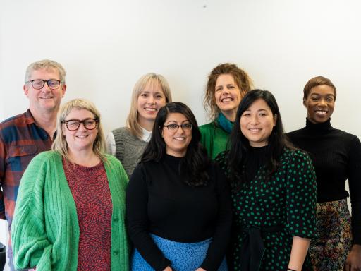 Seven people stand in front of a white background, smiling