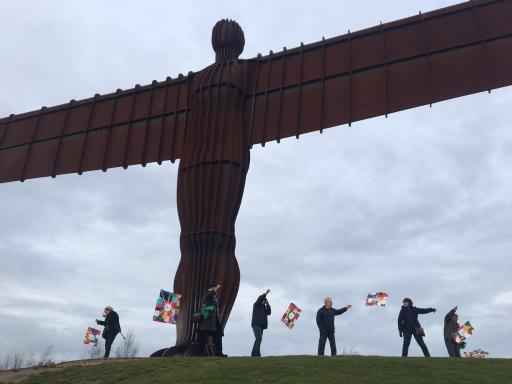 People flying their handmade Korean kites with Equal Arts under the Angel of the North statue against a grey sky