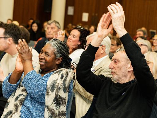 People clapping enthusiatically in an audience at an event - one clapping their hands over their head 