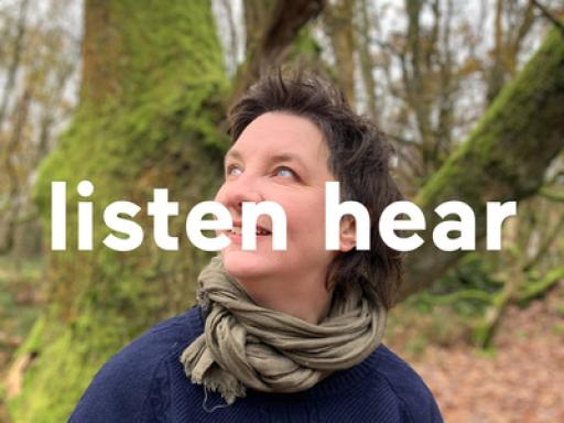 a person looks up to their right, standing in the woods, wearing a blue jumper and a green scarf, with the words 'listen here' across the centre of the image