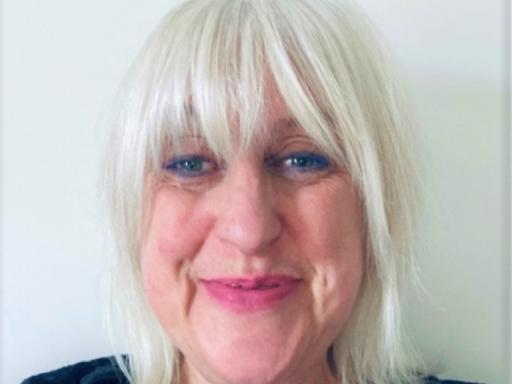 Close up photograph of middle aged white woman with shoulder length white hair wearing a navy blue round neck top