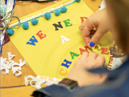 A person making a colourful banner that reads 'We Need A Change'