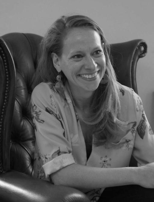 B&W photograph of a white woman with long mousey blonde hair smiling sitting in a chair