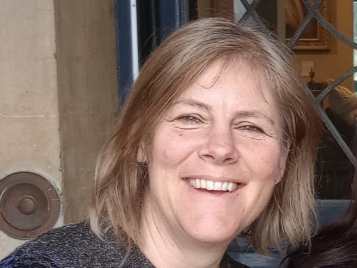 close-up photo of a person with medium-length blond hair smiling ino the camera with a door frame behind them