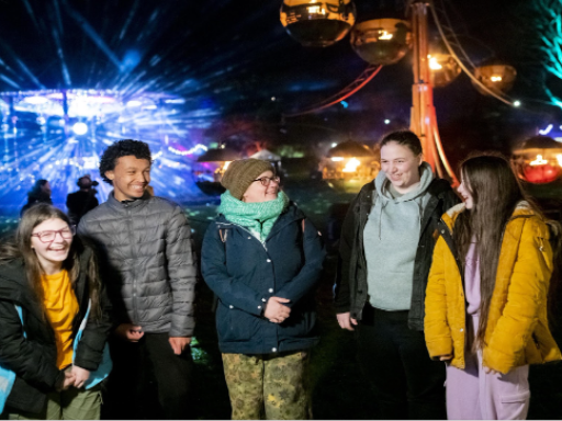 5 people stand smiling in front of a light display, outside at night