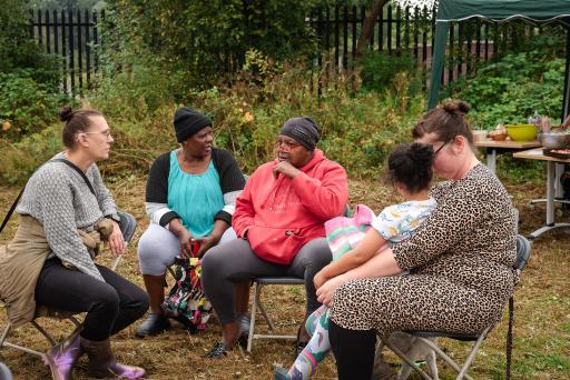 A group of women and a child sit in a circle outdoors talking to each other