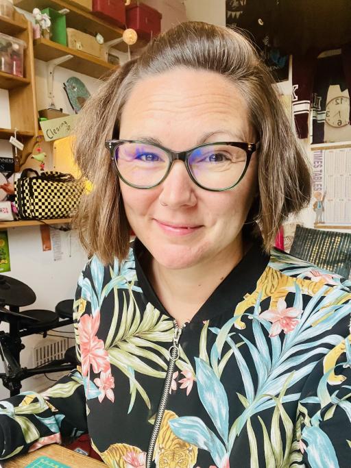A woman with short brown hair wearing black glasses and a floral shirt smiling 
