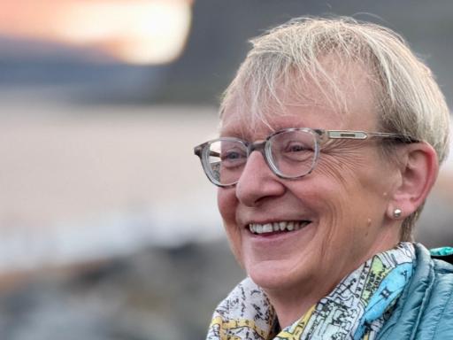 portrait of a woman with short blonde hair and glasses smiling, on a beach