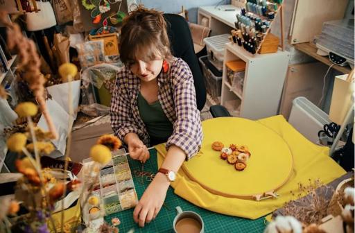 A woman sitting at a table with boldly coloured cloth embroidering