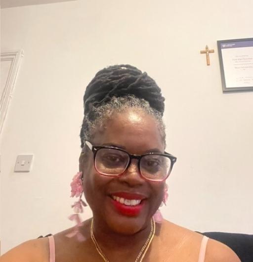 A black woman wearing red lipstick and black glasses with her locs up in a bun, smiling at the camera against a white background